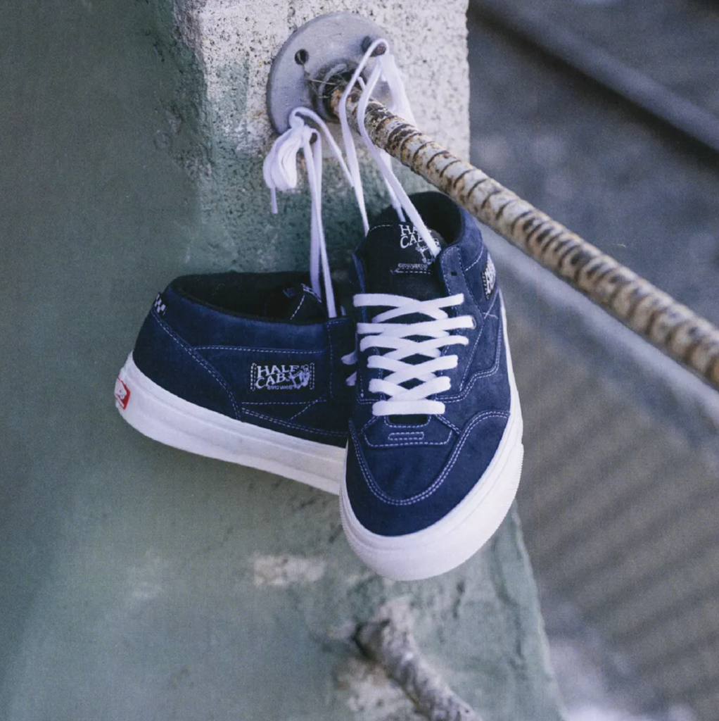 A pair of blue Vans Skate Half Cab Dress Blues sneakers, perfect for skateboarding, hanging on a railing.