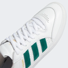A pair of white and green Adidas Tyshawn Low Flat White/Collegiate Green/Metallic Gold sneakers on a white background.