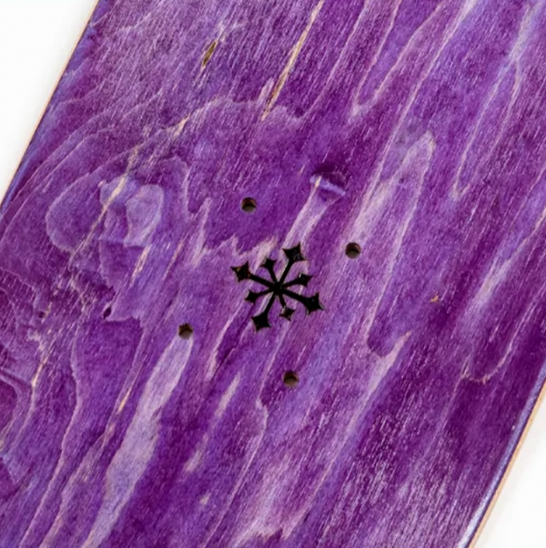 Close-up of the DISORDER JAH skateboard deck from Disorder, showcasing a purple wooden finish with a black cross-shaped design and several small holes for truck mounts, alongside an eye-catching Nyjah graphic.