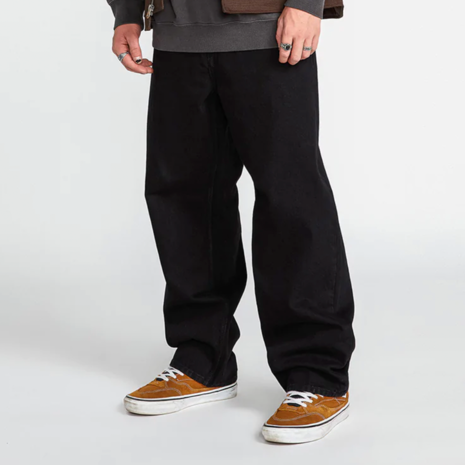 A man wearing a VOLCOM BILLOW DENIM LOOSE FIT BLACK jacket and black pants.