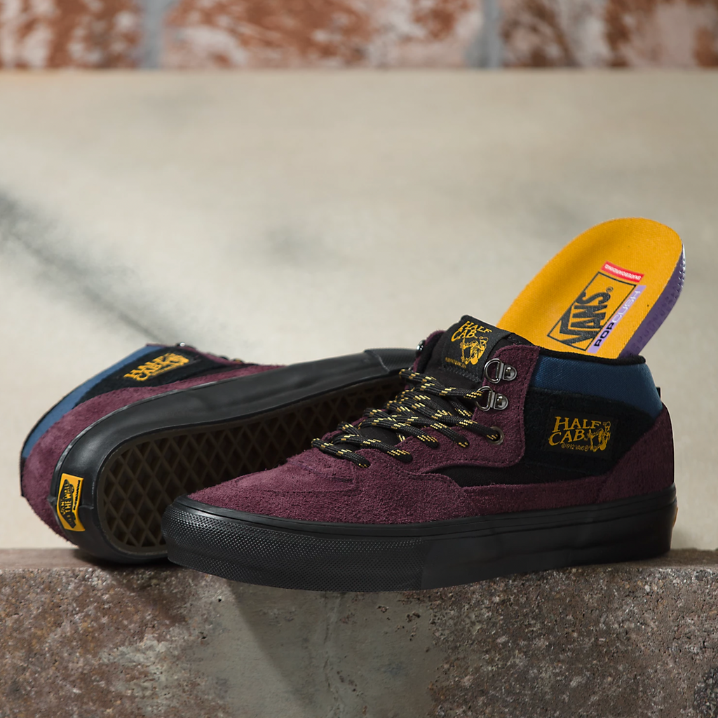 A pair of VANS SKATE HALF CAB OUTDOOR PURPLE / BLACK shoes sitting on top of a cement wall.