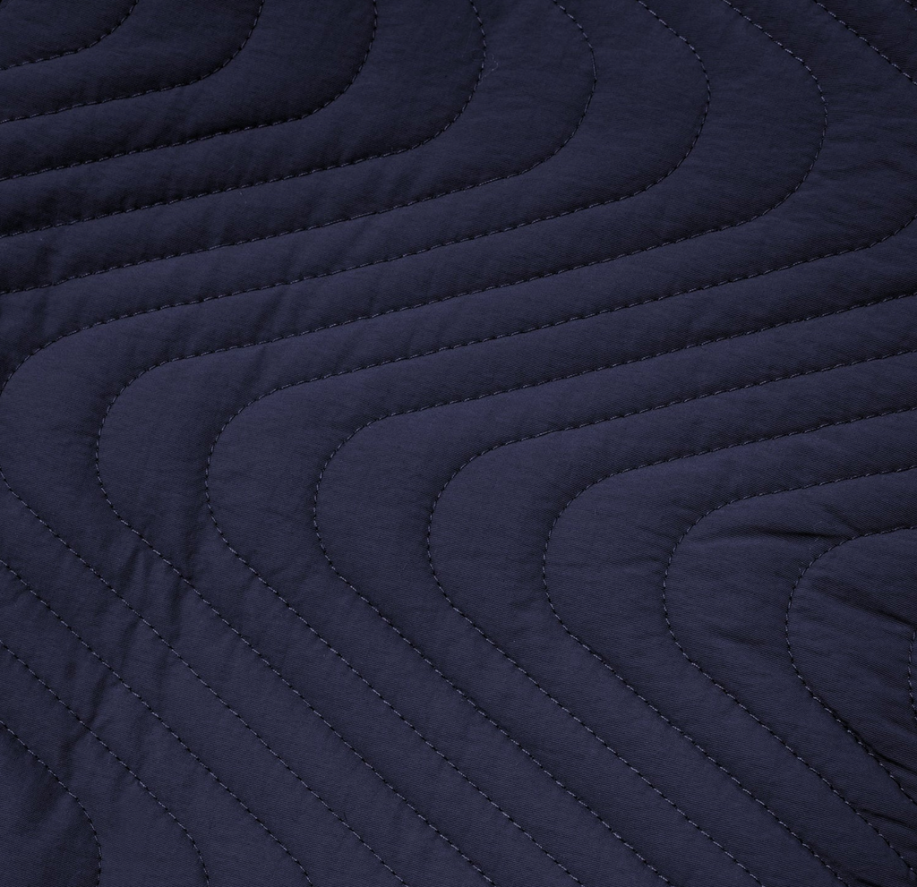A close up of a Butter Goods quilted reversible jacket in navy/blue on a bed.
