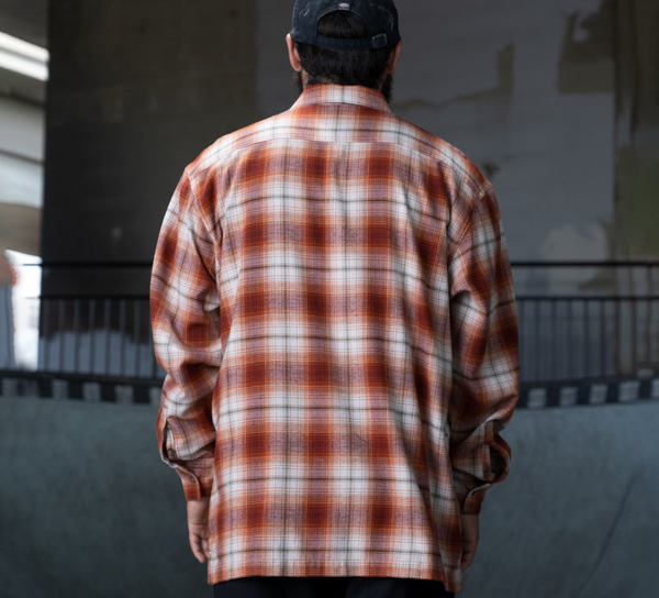 A man in a DICKIES RONNIE SANDOVAL BRUSHED FLANNEL SHIRT BURNT OMBRE is looking at a skateboard.