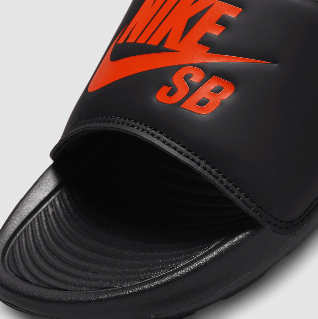 A pair of black and orange Nike SB Victor One slides.
