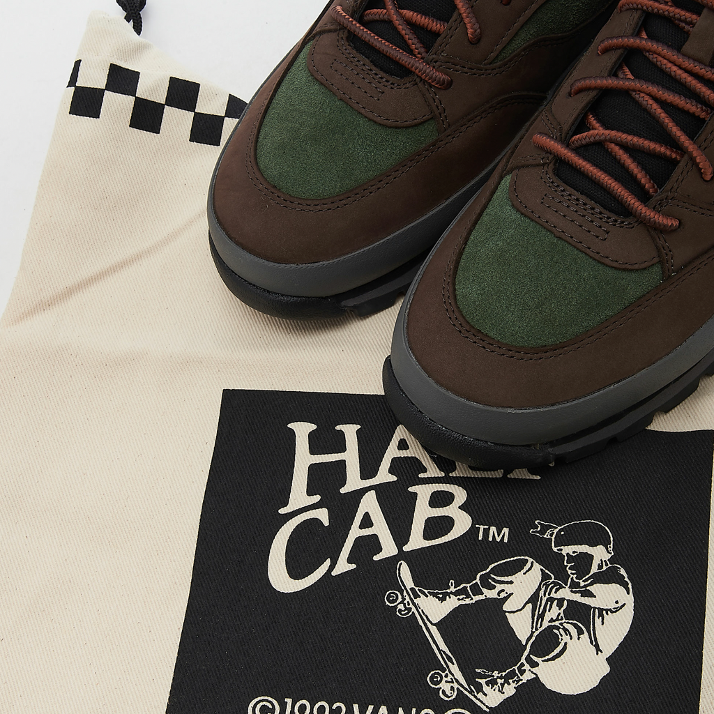 A pair of brown and green VANS SKATE X TIMBERLAND HALF CAB HIKER GREEN / BROWN sneakers on top of a bag.