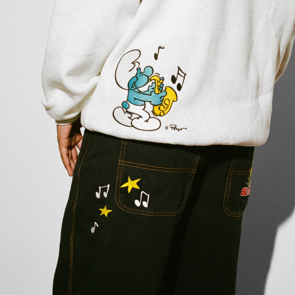 A person wearing Butter Goods' Harmony Denim Pants with The Smurfs cartoon character on them.