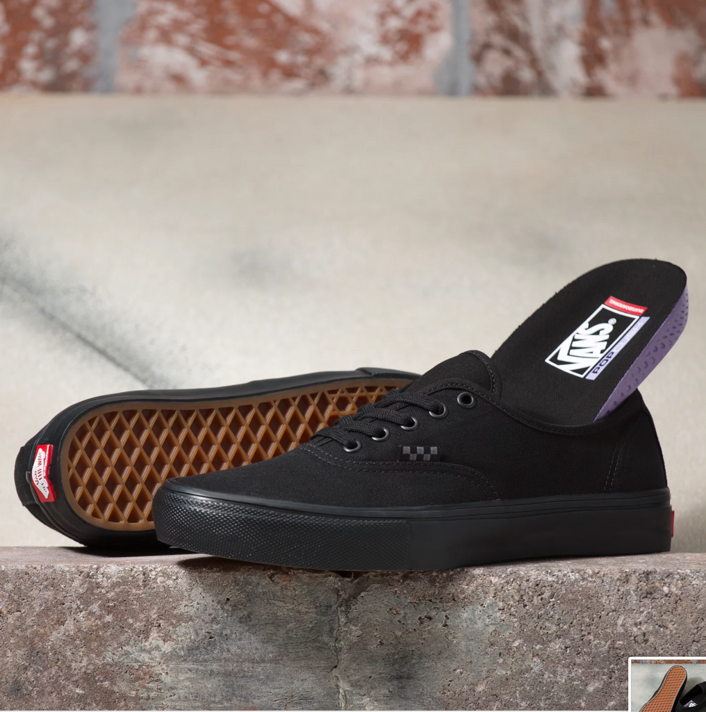 A pair of VANS SKATE AUTHENTIC BLACK / BLACK shoes sitting on top of a stone wall.