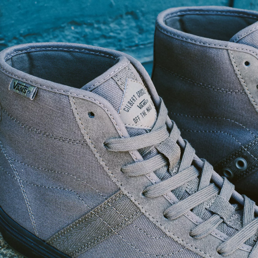 A pair of grey VANS CROCKETT HIGH BUNGEE CORD / BLACK sneakers on a brick wall.