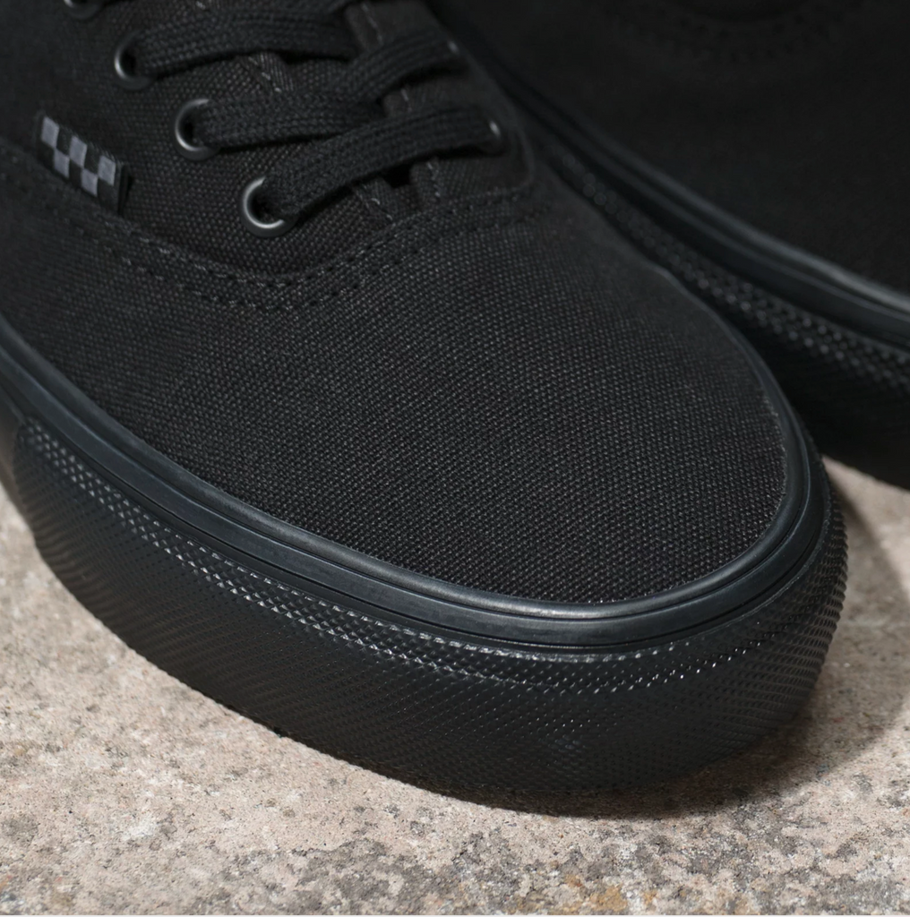 A pair of VANS SKATE AUTHENTIC BLACK / BLACK shoes sitting on top of a stone floor.