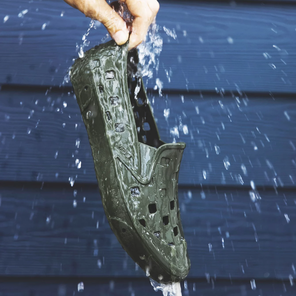 A person holding a VANS TREK SLIP ON GRAPE LEAF shoe in the rain.