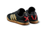 A pair of black and gold ADIDAS BUSENITZ INDOOR SUPER BLACK/GOLD/SCARLET shoes on a white background.