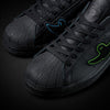A pair of ADIDAS x GONZ SUPERSTAR ADV CORE BLACK / BLACK / BLACK sneakers on a black background.