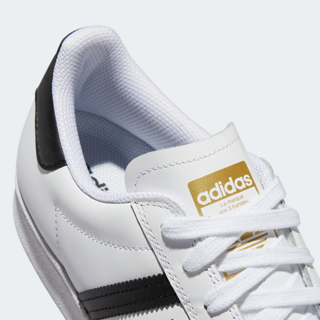 A white ADIDAS SUPERSTAR ADV FLAT with a black and gold stripe.