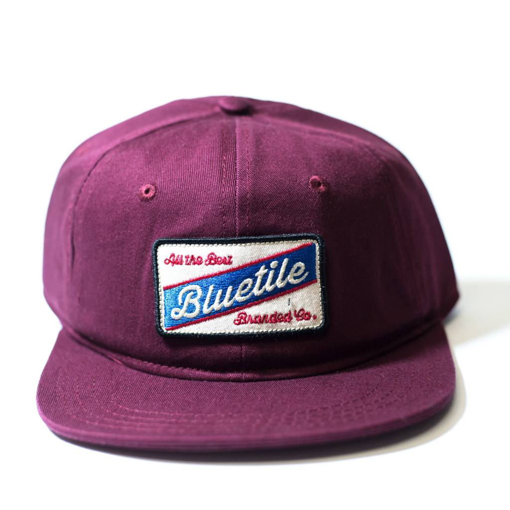 A vibrant BLUETILE "ALL THE BEST" COLOR PATCH GARNET hat featuring a striking blue and white patch from Bluetile Skateboards.