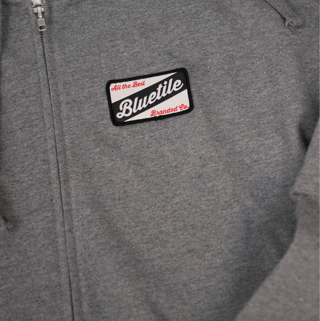 A Bluetile Skateboards zip hoodie with a patch on it.