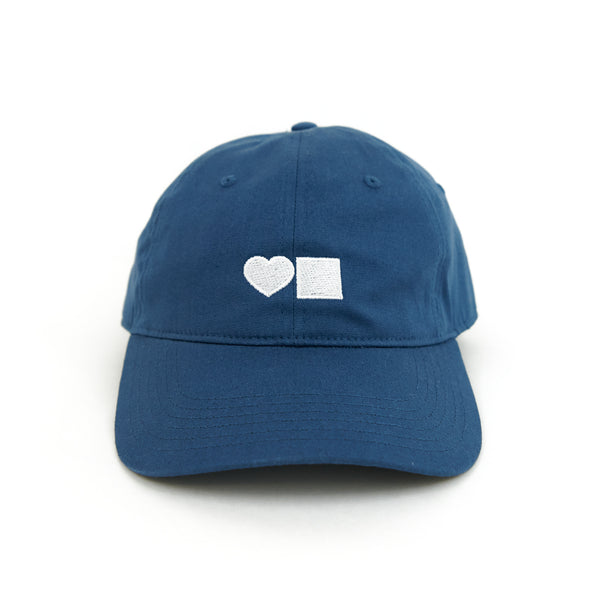 A BLUETILE LOVE SIX PANEL HAT HARBOUR BLUE with a white heart on it.