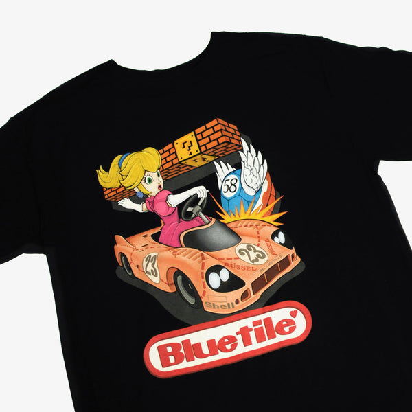 A BLUETILE LAST LAP T-SHIRT BLACK with an image of a girl driving a car on the last lap, made by Bluetile Skateboards.