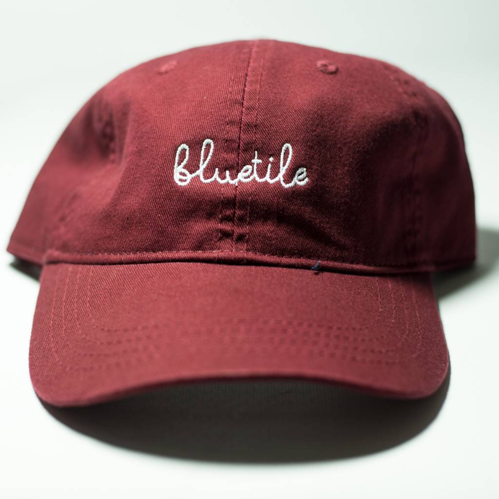 A BLUETILE SCRIPT DAD HAT GARNETT with the word 'bluetle' embroidered on it, made by Bluetile Skateboards.