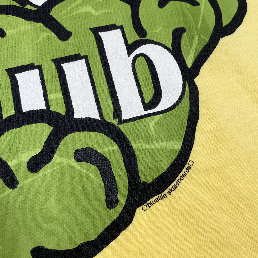 A yellow BLUETILE GARDEN CLUB TEE BUTTER with a green logo on it, designed for Bluetile Skateboards.