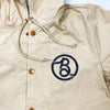 A Bluetile Skateboards coaches jacket in bone with a blue b logo on it.