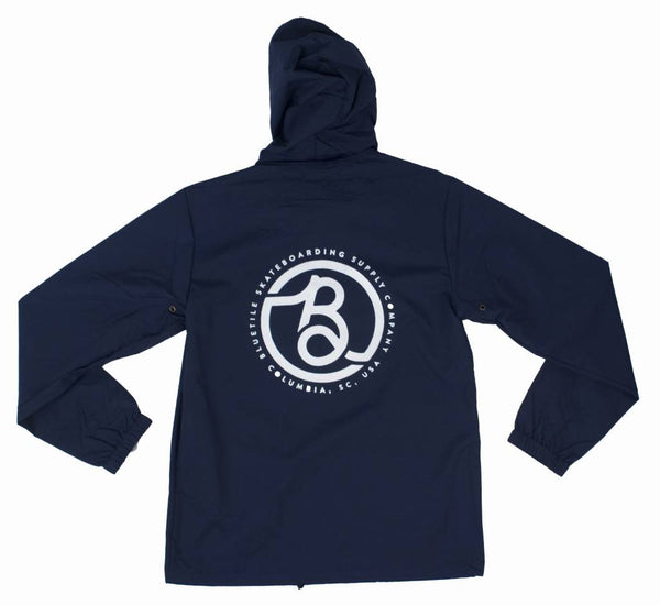 A BLUETILE SUPPLY CO HOODED COACHES JACKET (NAVY) with a white logo on it.