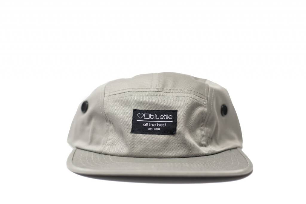 An adjustable BLUETILE SURPLUS 5 PANEL HAT LIGHT GRAY with a black patch on it, made by Bluetile Skateboards.