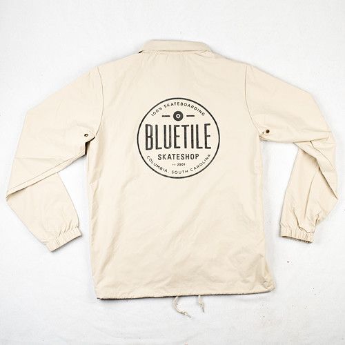 A beige BLUETILE SINCE 2001 REFLECTIVE INK COACHES JACKET with a black logo on it by Bluetile Skateboards.