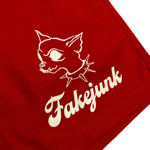The FAKE JUNK CHI CHI BEACH SHORTS RED by FAKE JUNK feature a red fabric with a white print of a stylized cat head wearing a spiked collar and the word "Fakejunk" in cursive, perfect for your pool skating adventures.