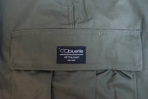 A close up of a BLUETILE SURPLUS CARGO PANT OLIVE jacket with Poly/Cotton Twill fabric and utility pockets.