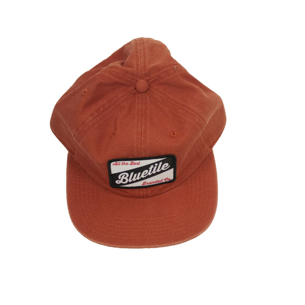 A BLUETILE CRAFT PATCH HAT COPPER with a Bluetile Skateboards patch on it.