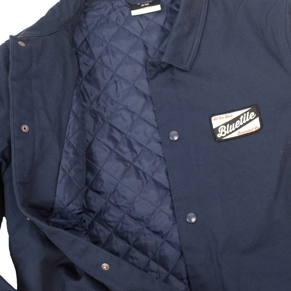 A navy BLUETILE Craft mechanic jacket with a patch on the back and Quilted lining (Brand Name: Bluetile Skateboards).