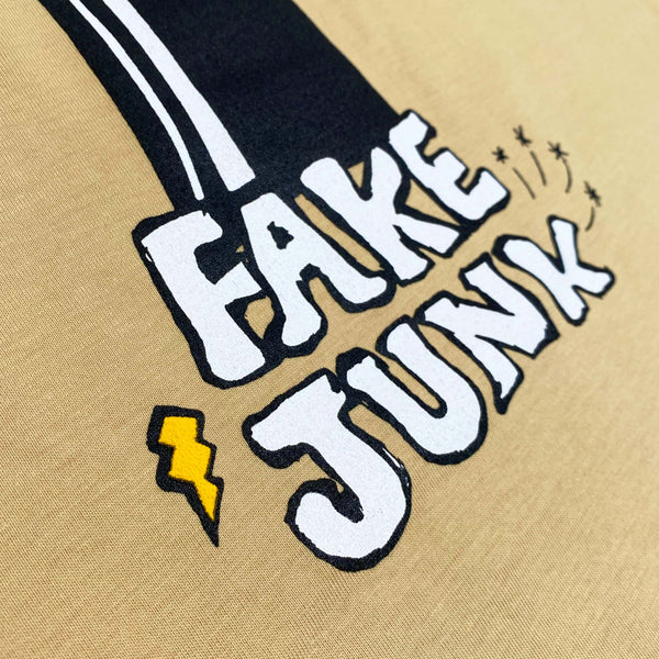 Close-up of a screen print on the FAKE JUNK B.U.N.N.Y T-SHIRT TAN featuring the text "FAKE JUNK" in bold white letters outlined in black, with a lightning bolt below and small stars to the right of the text.