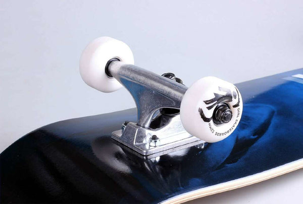 Close-up of the GIRL MALTO NIGHT ATTACK COMPLETE 8.25 skateboard by GIRL, highlighting its trucks and white wheels on a dark blue deck against a plain background.