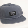 A BLUETILE SUPPLY PATCH HAT PETROL BLUE with a black patch on it. (Brand: Bluetile Skateboards)