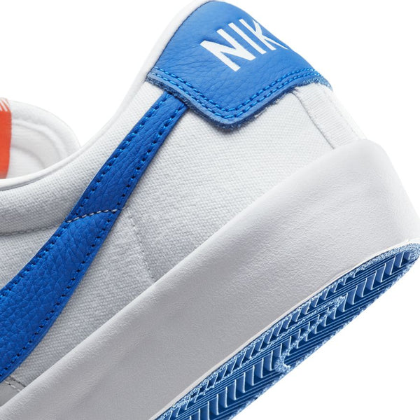 Close-up of a white nike NIKE SB BLAZER LOW PRO GT ISO WHITE / VARSITY ROYAL sneaker with blue accents, including a blue sole, blue leather heel tab, and part of the nike logo visible on the heel.