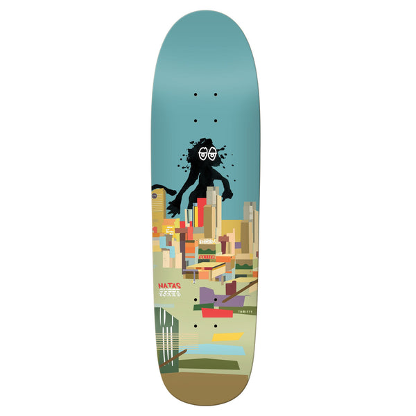 The KROOKED NATAS ART BY NATAS skateboard deck by KROOKED features iconic Natas art—a black cartoon monster with glasses over abstract city buildings, set against a blue sky.