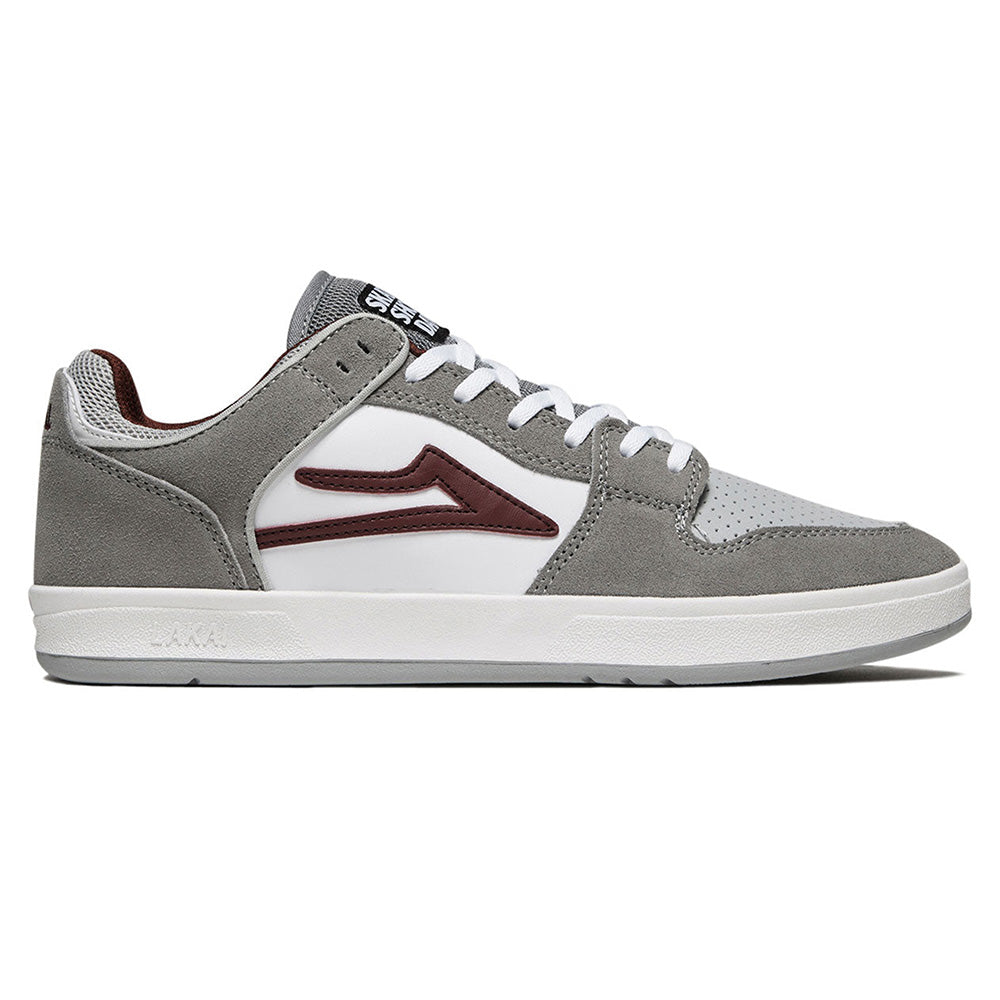 The LAKAI X SKATE SHOP DAY TELFORD LOW by LAKAI is a stylish skate shoe with a sleek grey and maroon design adorned with a white and maroon logo.