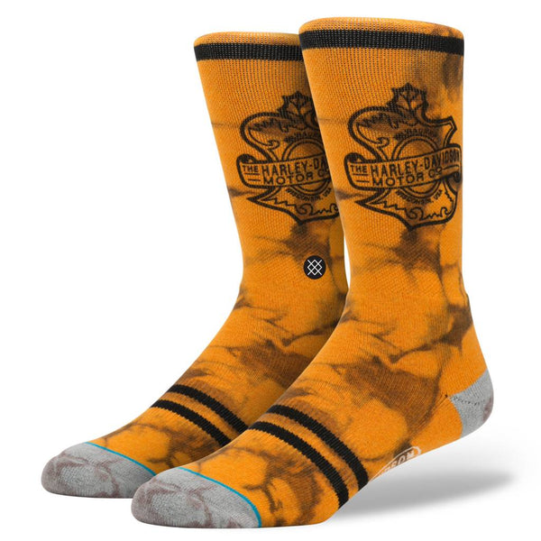 The STANCE SOCKS HARLEY DAVIDSON by STANCE are orange and black tie-dye crew socks with grey toes and heels, black stripes near the cuffs and toes, and feature the Harley-Davidson logo.
