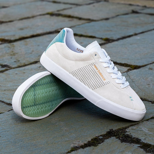 A pair of NB NUMERIC 22 X LOST ART GREY sneakers on a cobblestone.