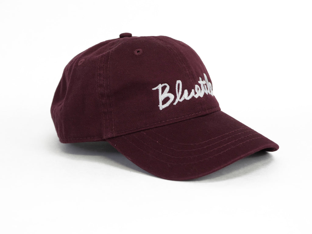 A BLUETILE CURSIVE DAD HAT MAROON with the word 'blush' embroidered in cursive.