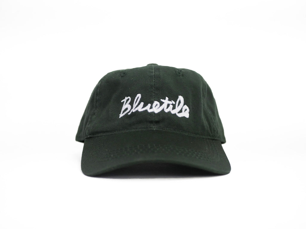 A BLUETILE CURSIVE DAD HAT FOREST GREEN with the word blues written on it.