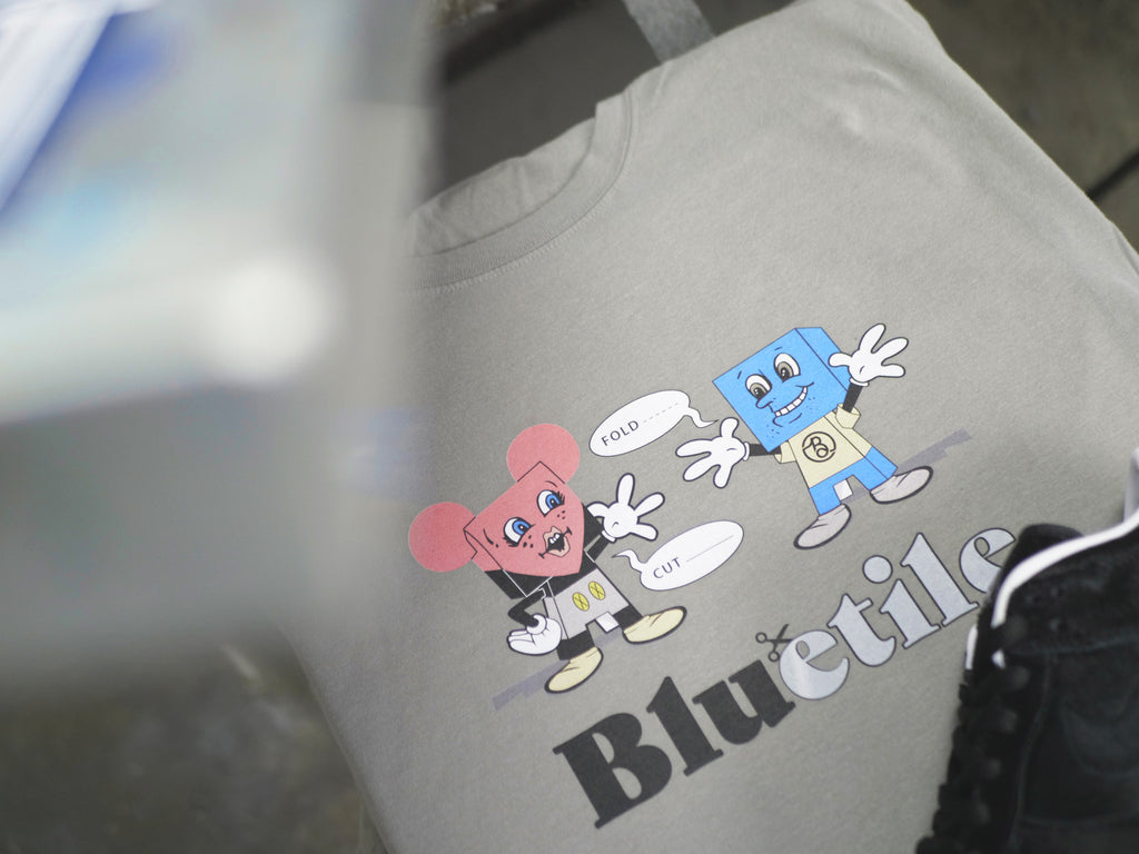 A BLUETILE PAPER TOYS T-SHIRT GREY with a cartoon character on it.