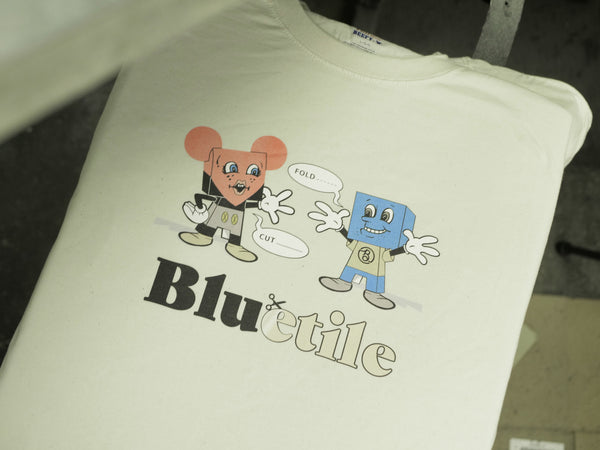 A BLUETILE PAPER TOYS T-SHIRT NATURAL by Bluetile Skateboards featuring two cartoon characters wearing blue tile patterned paper toy outfits.