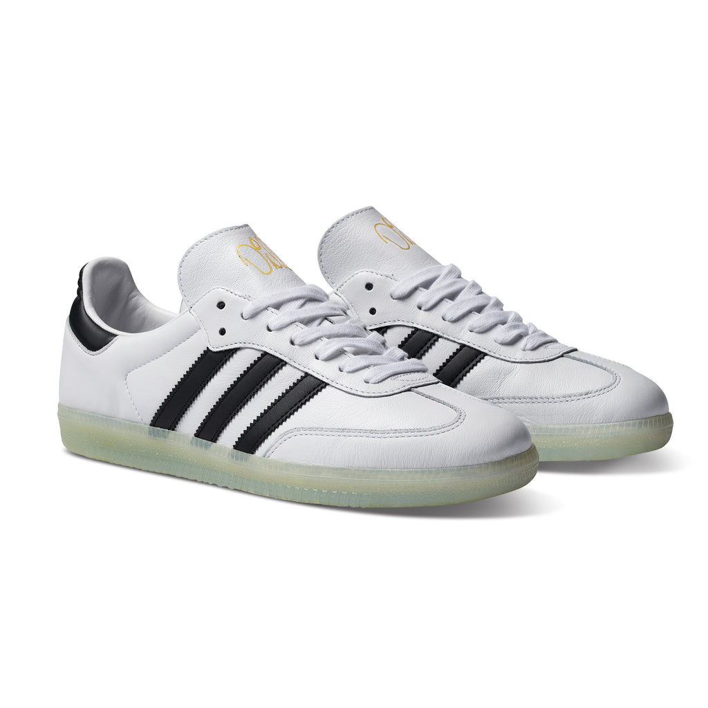 A black and white ADIDAS JASON DILL SAMBA WHITE / CORE BLACK / GOLD METALLIC sneakers with black stripes.