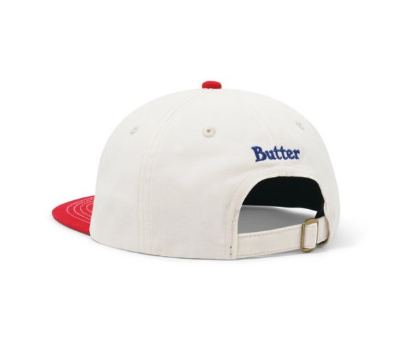 The Butter Goods Apple 6 Panel Cap in Natural/Cherry features a white crown, red brim and back strap, with "Butter" embroidered in blue above the opening.