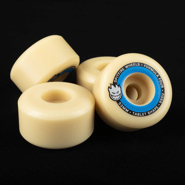 On a black surface lie four SPITFIRE FORMULA FOUR TABLETS wheels, 51mm in size and beige in color, featuring blue and black Spitfire Wheels logos.