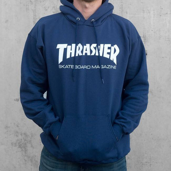 A person wearing the THRASHER SKATE MAG LOGO HOODIE with the "Thrasher Skateboard Magazine" text on the front. The person has their hands in the hoodie pocket, standing against a plain gray background.