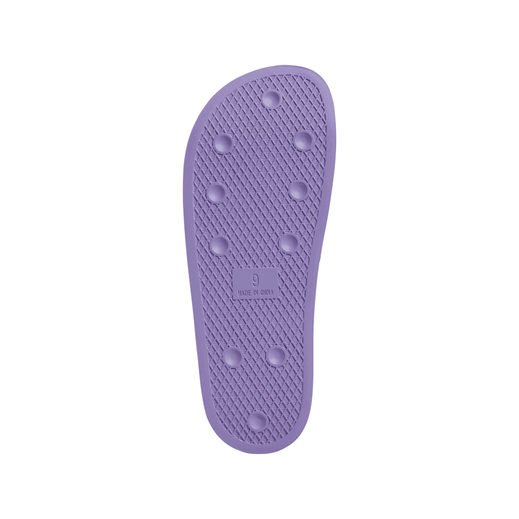 A close up of an ADIDAS SHMOOFOIL SLIDE LILAC/WHITE shoe cover on a green background.