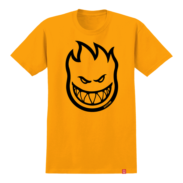 A gold SPITFIRE BIGHEAD TEE from DELUXE featuring a large, stylized black graphic of a grinning face with spiky hair.