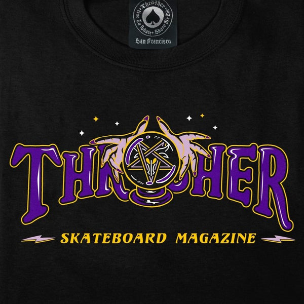 A black THRASHER FORTUNE LOGO TEE featuring the words "Thrasher Skateboard Magazine" in vibrant purple and yellow, accompanied by an illustrated flaming skateboard wheel.